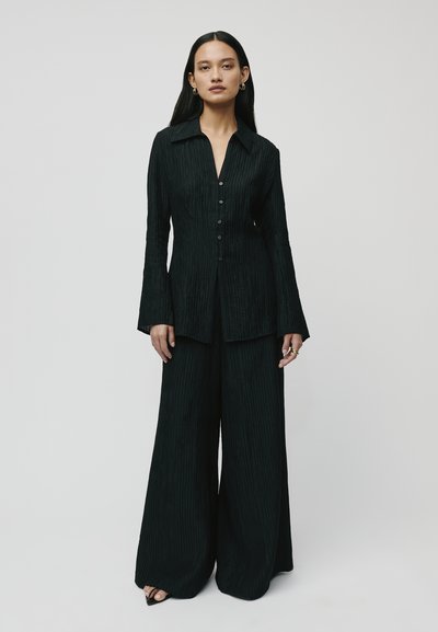 Black ribbed two-piece outfit featuring a long-sleeve button-up shirt and wide-leg pants, textured fabric, and subtle sheen.