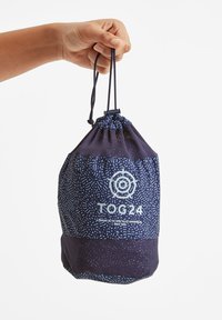 Navy drawstring bag features a textured pattern and a solid lower section. Includes a white logo and handle for easy carrying.