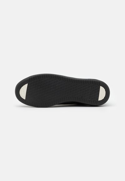 Black rubber shoe sole with a textured surface, featuring a white accent at the toe. The design includes a diamond pattern for traction.