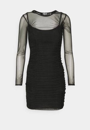 Robe bodycon noire froncée avec manches longues et encolure transparentes, présentant un col rond et une silhouette ajustée.
