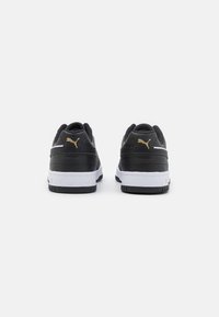 Sneaker sintetiche nere con suole bianche, caratterizzate da un logo oro, collo imbottito e una superficie liscia. Design classico a basse top.