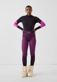 Completo atletico a tutto corpo in nero e viola, con maniche lunghe, colletto alla coreana e motivi a righe. Abbinato a stivali beige isolanti.