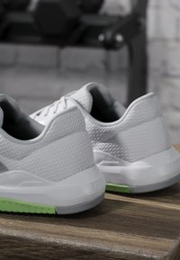 Paire de chaussures de sport blanches avec tissu texturé et semelles vert clair posées sur une surface en bois.