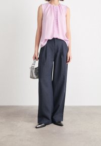 Blusa sin mangas de color rosa con un frente plisado, combinada con pantalones holgados de color marino. Los accesorios incluyen un pequeño bolso plateado y zapatos negros de punta.