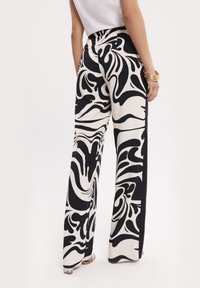 Czarno-białe spodnie o szerokich nogawkach z wirującym, abstrakcyjnym wzorem, gładki materiał, wysoki stan i widoczne szwy boczne.