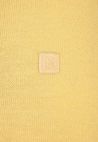 Tessuto di maglione giallo realizzato a maglia con una finitura testurizzata. Presenta un'etichetta quadrata in pelle beige con un logo "M" in rilievo.