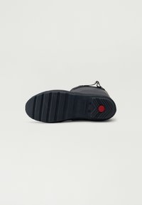 Suela de bota de goma negra con un diseño de banda de rodadura patrón; incluye un acento rojo cerca del talón y marca en la parte inferior.