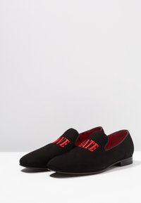 Zwarte suède instappers met een spitse neus, voorzien van rode geborduurde tekst "LOVE" en "HATE" aan de voorkant. Rode binnenvoering, lage hak.