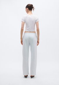 Valge lühike t-särk koos heledate hallide, lahtiste dressipükstega. Modellil mustad kontsakingad. Taust on lihtne ja hele.