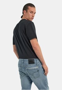 T-shirt nero a maniche corte abbinato a jeans azzurri chiari con leggera scoloritura, taglio dritto e un'etichetta di marca visibile sul cinturino.