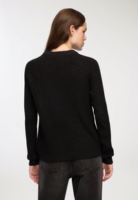 Maglione nero lavorato a maglia con un motivo testurizzato, con polsini e orlo a coste. Presenta un classico colletto a girocollo e una vestibilità rilassata, abbinato a jeans scuri.