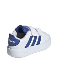 Zapatilla blanca con acentos azules, que presenta tres rayas azules, correas de Velcro y una suela texturizada. Fabricada en material sintético.