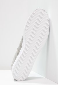 Grå sneakers med en texturerad ovandel, med en gummisula med ett zigzag-mönster och en vit mellansula.