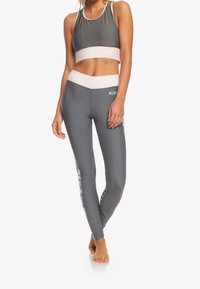 Szary sportowy crop top z kontrastującym różowym pasem; dopasowane legginsy z akcentami w kamuflażu po bokach. Miękka, elastyczna tkanina.