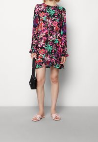 Vestido floral con mangas largas, fondo negro, patrones en rosa y verde; combinado con un bolso negro y sandalias planas rosas con nudo.