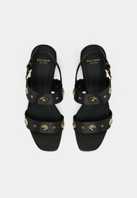 Black leather sandals with gold floral embellishments, adjustable ankle strap, flat sole, and textured footbed. Brand logo visible on insole.