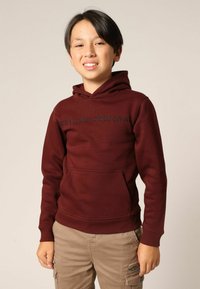 Sweat à capuche bordeaux avec une poche avant, arborant le texte "Eeluxe Original" en noir sur la poitrine. Tissu doux et texturé.