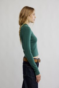 Grønn ribbestrikket genser med kort design og lange ermer, kombinert med mørkeblå denimjeans og et brunt belte.