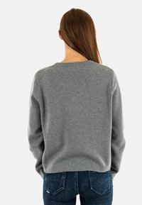 Maglione grigio a maglia con scollatura rotonda e maniche lunghe, abbinato a jeans in denim blu scuro. Texture liscia, vestibilità casual.