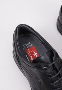 Scarpa in pelle nera con superficie testurizzata, design con lacci e soletta imbottita etichettata "Light 1/2 Peso" di Fluchot.