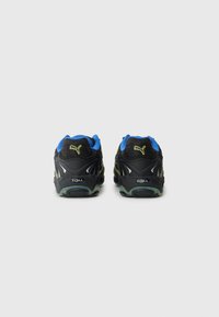 Ett par svarta Puma löparskor med blå inredning och gul logotyp, sedd bakifrån på en enkel ljusgrå bakgrund.