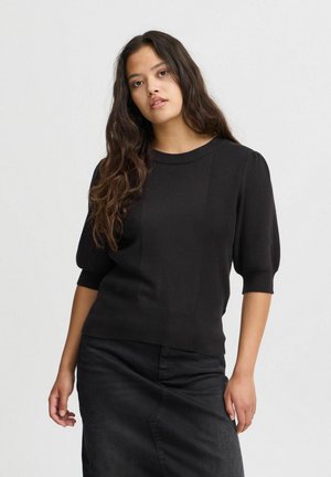 Maglione nero lavorato a maglia con maniche a sbuffo corte, texture a coste e collo rotondo. Abbinato a una gonna scura.