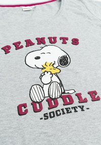 T-shirt grigia con una grafica in bianco e nero di Snoopy che tiene un uccellino giallo. Il testo recita "PEANUTS CUDDLE SOCIETY" in viola e nero.