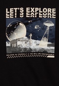 Camiseta negra con un diseño gráfico de una casa sobre una superficie similar a la luna, con planetas, OVNIs y el texto: "VAMOS A EXPLORAR" y "CREE EN TI MISMO."