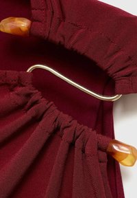 Tissu bordeaux avec une texture froncée, comportant un crochet métallique doré et deux accents en pierre couleur ambre sur les bords.