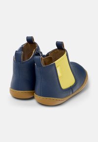 Une paire de bottes en cuir bleu marine pour tout-petits avec des panneaux élastiques jaunes sur les côtés et des semelles en caoutchouc beige, vues de l'arrière sur un fond blanc.