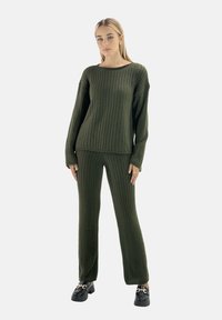 Olivgrönt ribbstickat set med tröja och byxor; långärmad, vid halsringning, avslappnad passform. Skorna har tjock sula och kedjedetalj.