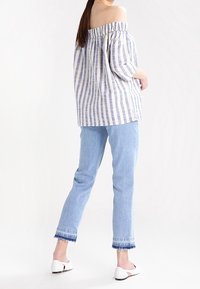 Haut rayé à épaules dénudées bleu et blanc, coupe décontractée, associé à un jean en denim clair avec ourlets effilochés et chaussures blanches.