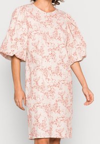 Kukkakuosiset mekko, jossa on pehmeä, teksturoitu kangas vaaleassa kermassa punaisilla kuvioilla; pyöreä pääntie ja runsaat lyhyet hihat.