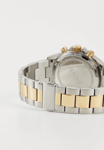 Montre en acier inoxydable avec un bracelet en argent et en or. Comprend trois boutons poussoirs dorés et un boîtier rond avec un fond en verre minéral.
