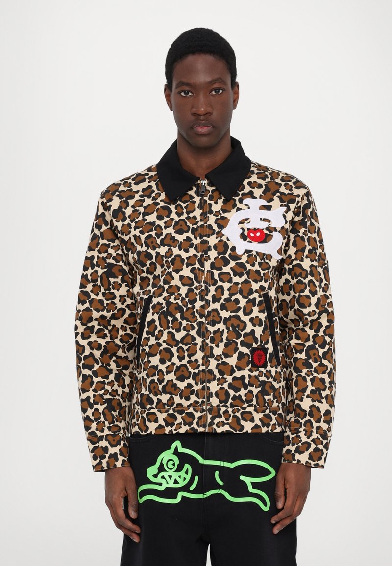 Giacca con stampa leopardata e colletto nero, caratterizzata da un accento rosso e un'etichetta con logo bianco. Il materiale sembra texturizzato e resistente.