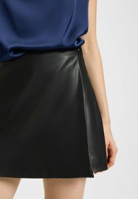 Black faux leather skort with an A-line silhouette, featuring a smooth texture and a side button closure. Paired with a blue satin top.