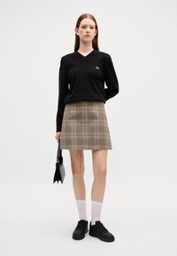 Maglione nero a V e mini gonna a quadri beige, abbinati a sneakers nere e calze bianche; con una borsa nera. Linee pulite, pattern classici.