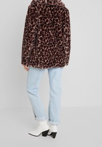 Chaqueta de piel sintética con estampado de leopardo de corte relajado, combinada con jeans azul claro con puños enrollados y botines blancos de tacón.