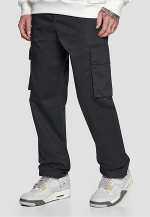 Person wearing black cargo pants and white sneakers standing with hands relaxed by sides against a plain background.