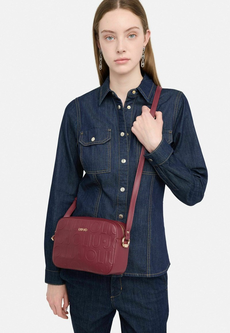 Borsa a tracolla color mogano in pelle testurizzata, con logo impresso, hardware dorato e tracolla regolabile.