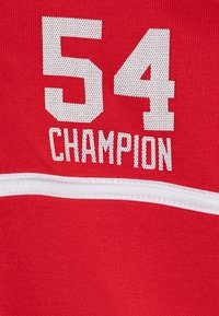 Crvena sportska majica s istaknutim bijelim brojevima "54" i tekstom "KAMPION", s bijelom horizontalnom prugom preko područja prsiju.