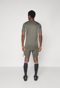 Idrettsantrekk med en mørkegrønn skjorte og shorts, med lysegrønne detaljer, svarte sokker og svarte fotballsko med gullfiner.