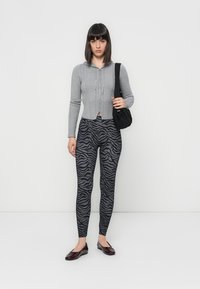 Gray knit zip-up cardigan, black and gray zebra-print leggings, and dark flats. Model holds a small black bag. Plain white background.