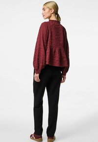 Blommefarvet bluse med tekstur, rynket halsudskæring, peplum-for, og lange ærmer, parret med sorte bukser og bordeaux sneakers. Enkel design.
