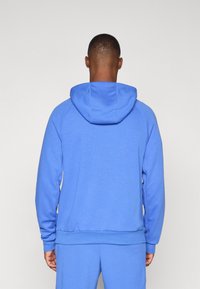 Blue hoodie with a drawstring hood, raglan sleeves, and a ribbed hem and cuffs. Soft fabric with a smooth texture. Back view shown.