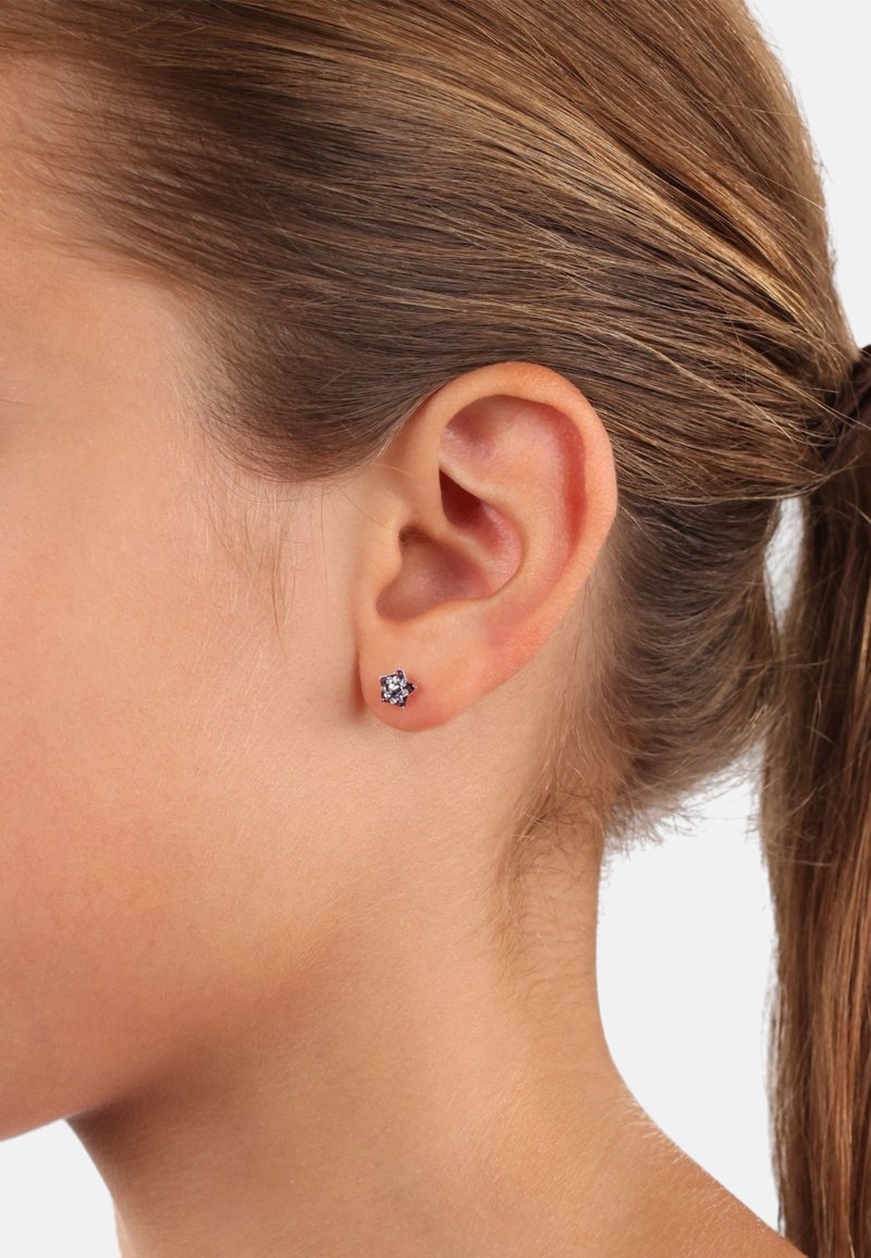 Orecchini a perno con design floreale e gemme viola incastonate nel metallo, indossati all'orecchio di una persona. I capelli sono raccolti. La pelle appare liscia.