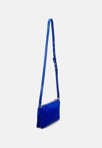 Blå crossbody taske lavet af blødt stof med en kviltet geometrisk design, udstyret med et slankt justerbart rem og guldlåse.