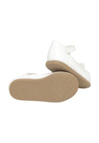 Zapatos de charol blancos con una sola tira de velcro, puntera redondeada, suela de goma beige texturizada y un sutil logo en la suela.