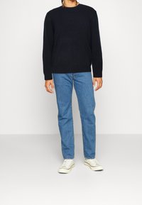 Pull noir en maille, col rond et poignets côtelés, associé à un jean droit bleu clair et des baskets blanches. Tenue simple et décontractée.