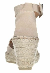 Beige espadrille wedge shoe with a smooth suede upper, ankle strap, and woven jute platform. Features a rounded toe and textured sole.